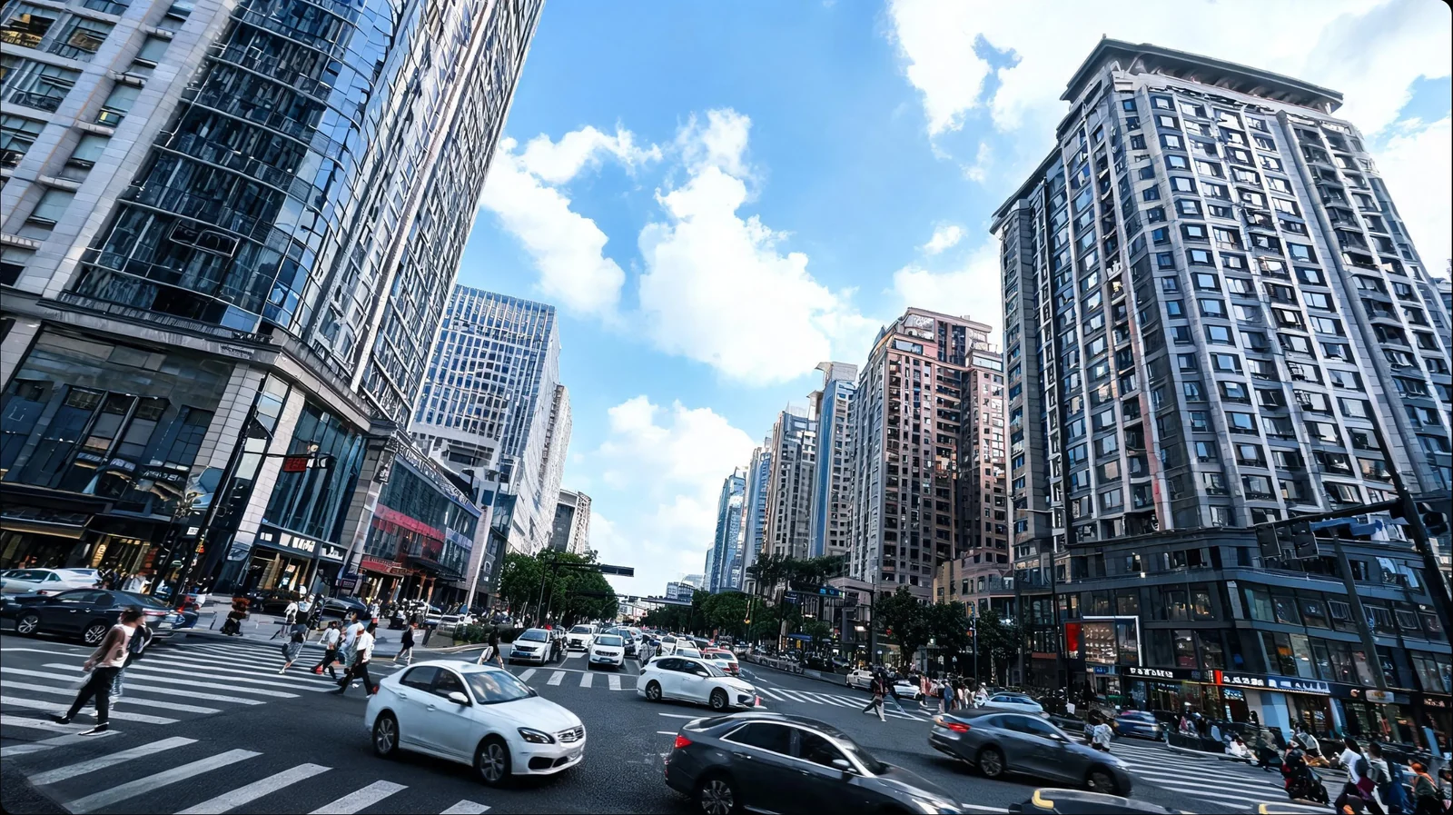 车辆与行人穿过城市十字路口，两侧高楼围住街道，蓝天白云出现在楼群之间。