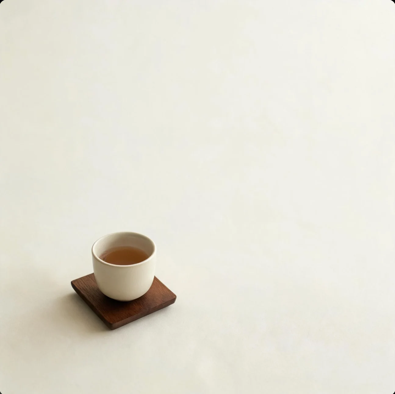 一只盛着棕色液体的白杯放在木杯垫上，周围是大面积浅色桌面。