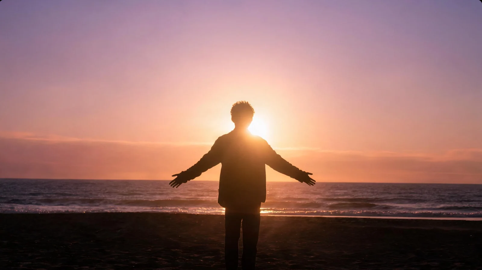 人物在海边张开双臂，夕阳位于身后，暗色轮廓映衬在橙粉色天空与海面前。